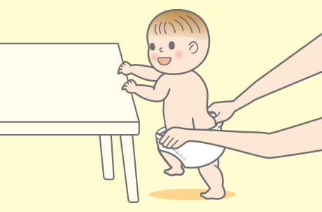 1. 前後を確認して、普通のパンツをはかせるのと同様に赤ちゃんをつかまり立ちをさせた状態にします。おむつの両脇を両手で広げ、赤ちゃんの足を通します。